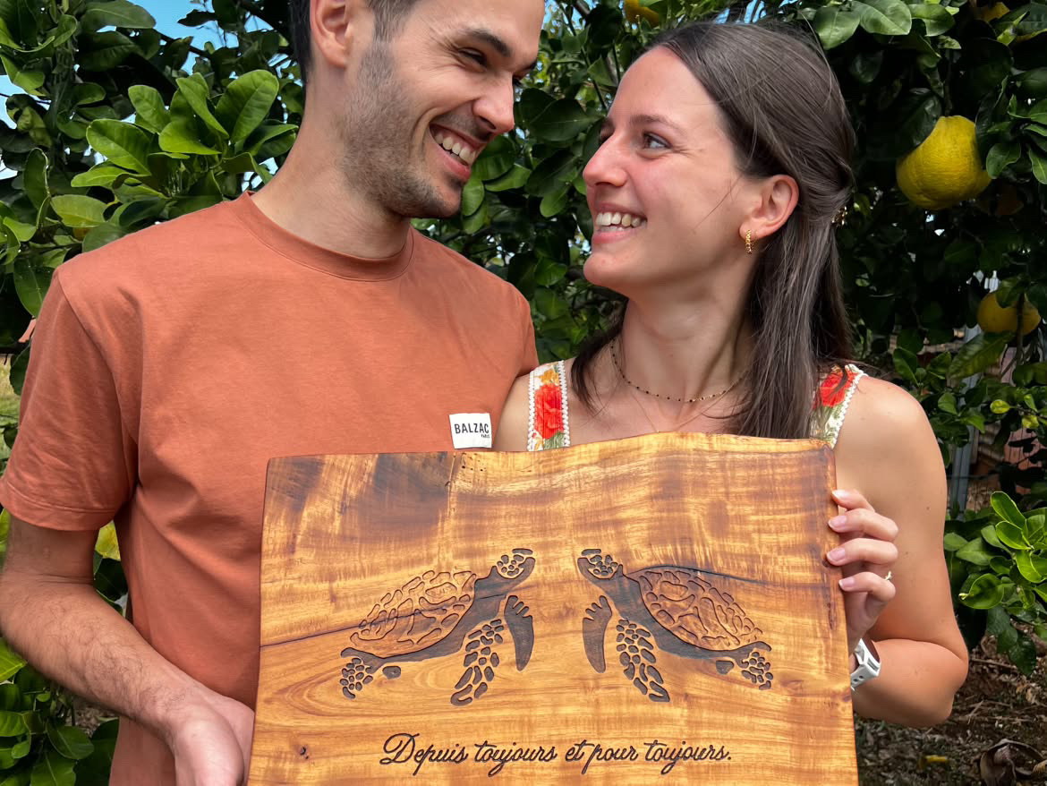 Un couple présente une planche en bois gravée de deux tortues